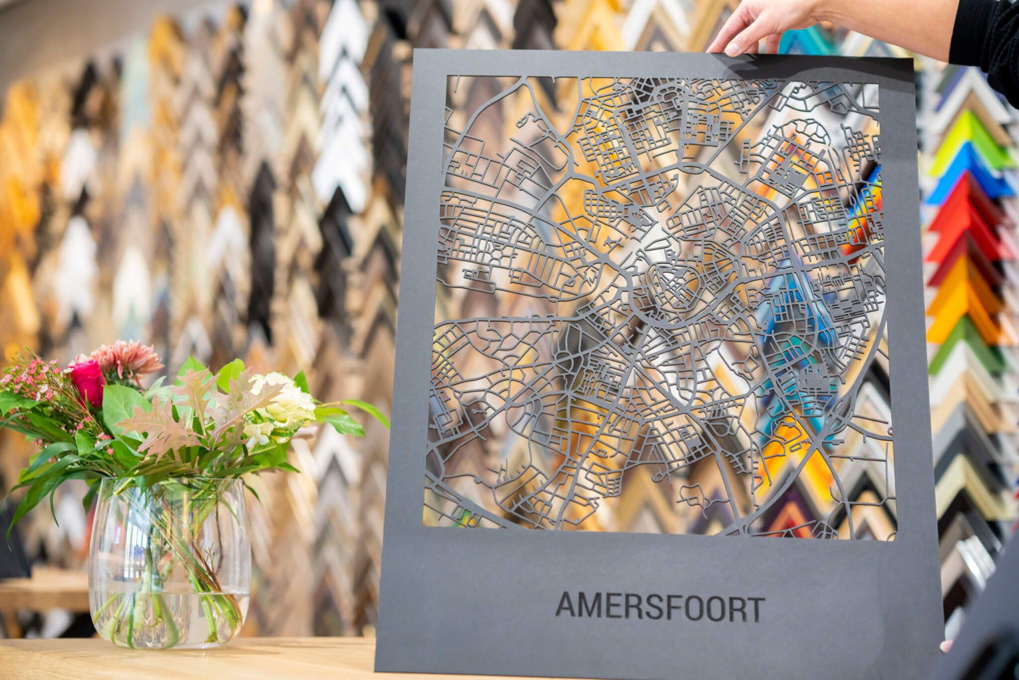 Een papercut kunstwerk van de plattegrond van Amersfoort, opgehouden tegen een wand met frameprofielen